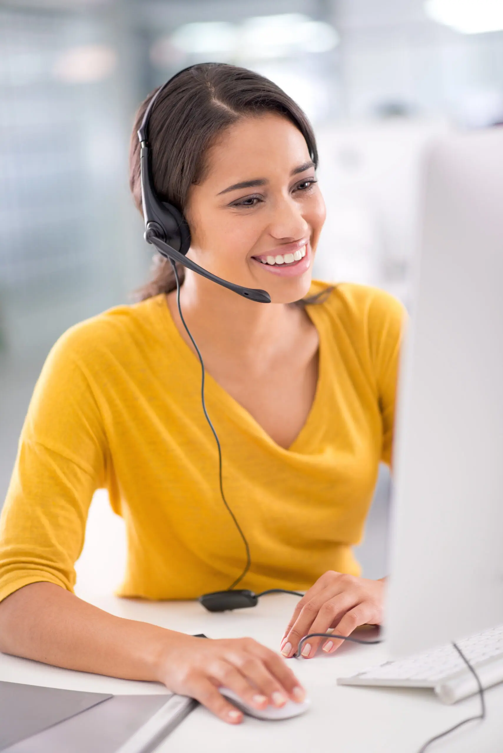 A smiling young customer service representative with a headset working at a computer, providing friendly support for Business process outsourcing solutions.